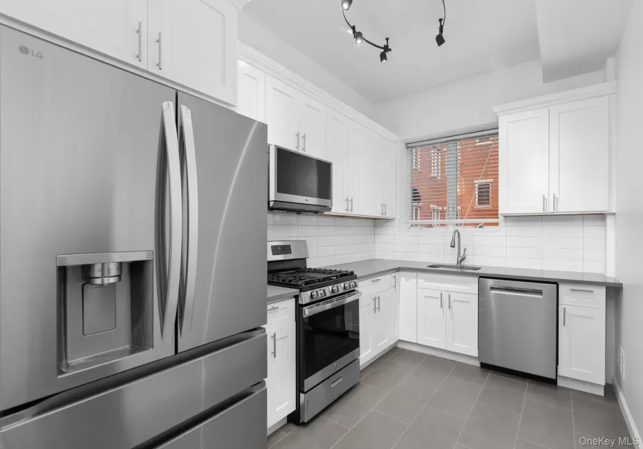 Kitchen featuring white shaker-style cabinetry, solid-surface countertops, subway tile backsplash, stainless steel appliances, and large-format tile flooring Kitchen featuring white shaker-style cabinetry, solid-surface countertops, subway tile backsplash, stainless steel appliances, and large-format tile flooring