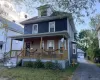 Two-story structure with blue siding, a covered front porch featuring wood-finish railings, and a dormer window Two-story structure with blue siding, a covered front porch featuring wood-finish railings, and a dormer window