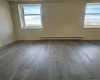 Empty room featuring dark wood-style floors, healthy amount of natural light, and baseboard heating Empty room featuring dark wood-style floors, healthy amount of natural light, and baseboard heating
