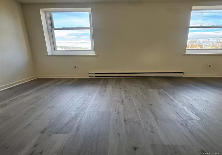 Empty room featuring dark wood-style floors, healthy amount of natural light, and baseboard heating Empty room featuring dark wood-style floors, healthy amount of natural light, and baseboard heating