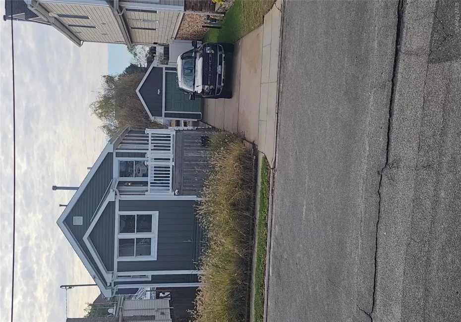 Dark-toned horizontal siding exterior featuring a front-facing wood deck with white railings, a detached garage, and a concrete driveway Dark-toned horizontal siding exterior featuring a front-facing wood deck with white railings, a detached garage, and a concrete driveway