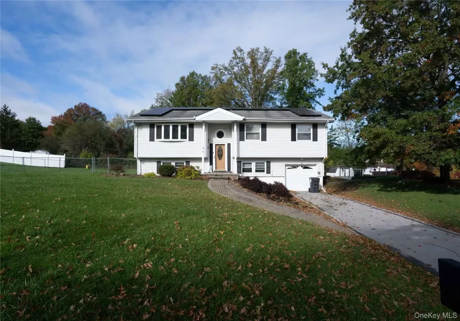 Split-level exterior featuring white siding, a paved driveway, attached garage, integrated solar panels, and a front entryway with a decorative window detail Split-level exterior featuring white siding, a paved driveway, attached garage, integrated solar panels, and a front entryway with a decorative window detail