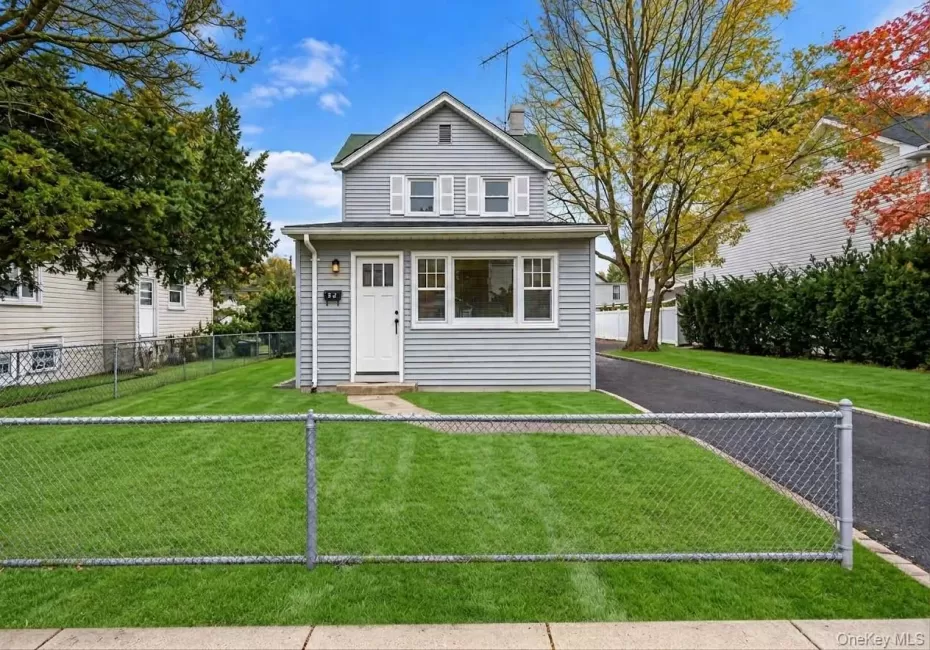 Two-story home with grey vinyl siding, white trim, a multi-pane front entry door, a paved driveway, and a chain-link fenced front yard *lawn and fence virtually edited Two-story home with grey vinyl siding, white trim, a multi-pane front entry door, a paved driveway, and a chain-link fenced front yard *lawn and fence virtually edited