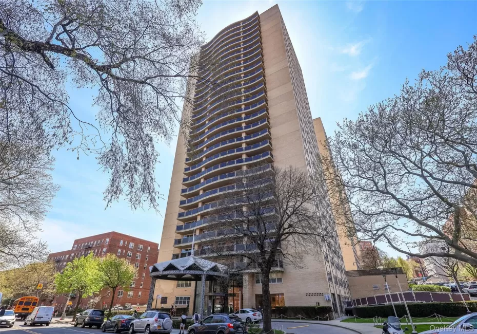 High-rise building exterior featuring a light-toned brick facade, curved balcony tiers, and a covered entrance canopy High-rise building exterior featuring a light-toned brick facade, curved balcony tiers, and a covered entrance canopy