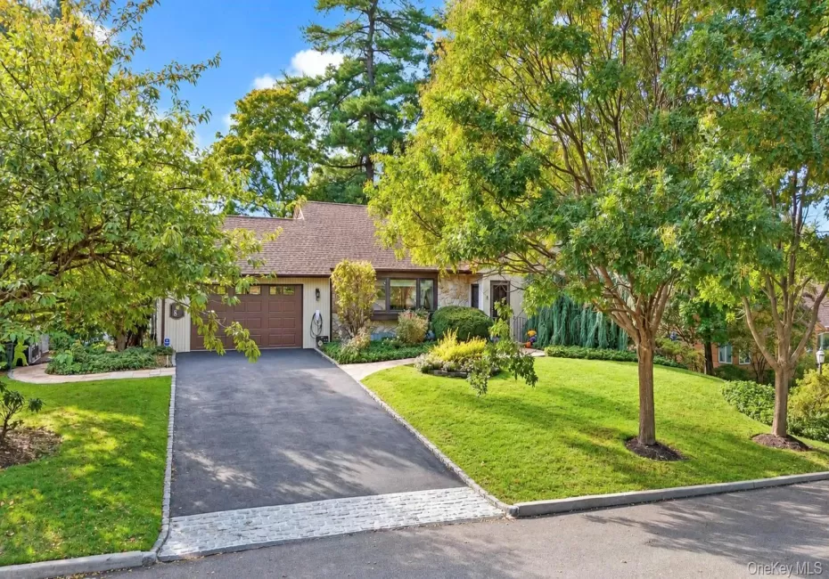 Asphalt driveway featuring a Belgian block apron, attached two-car garage, stone facade accents, and mature landscaping Asphalt driveway featuring a Belgian block apron, attached two-car garage, stone facade accents, and mature landscaping