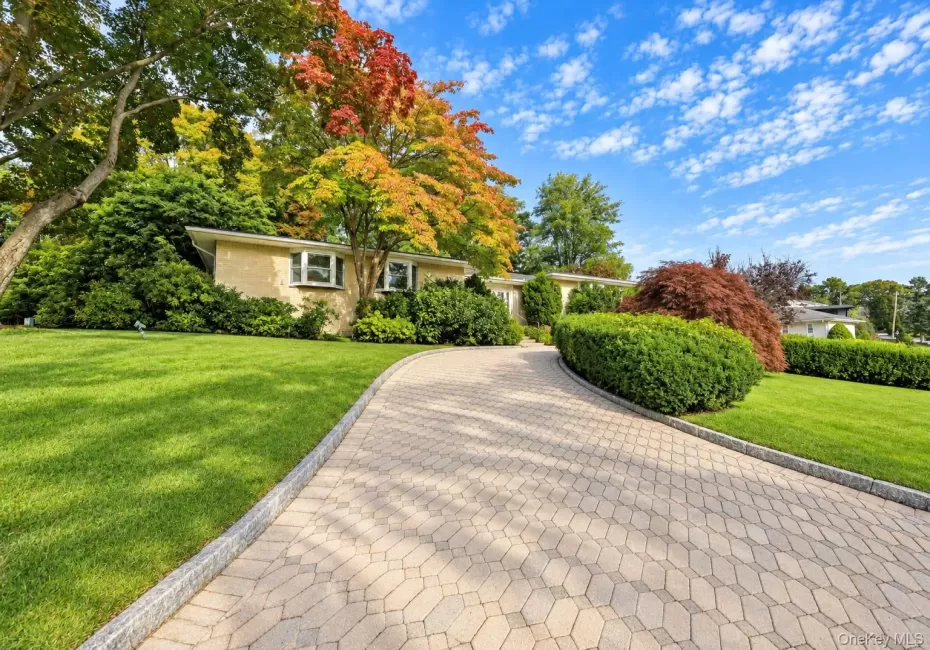 Brick exterior featuring a paved stone driveway, manicured landscaping, mature trees, and bay windows Brick exterior featuring a paved stone driveway, manicured landscaping, mature trees, and bay windows