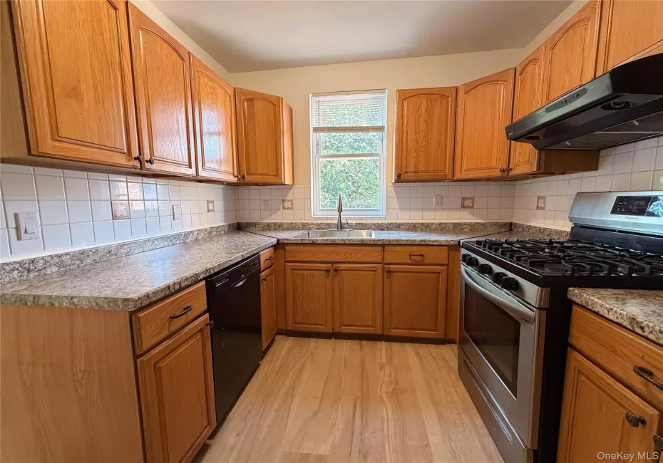Kitchen featuring natural wood cabinetry, stone-finish laminate countertops, white tiled backsplash, wood-finish flooring, and stainless steel gas range. Kitchen featuring natural wood cabinetry, stone-finish laminate countertops, white tiled backsplash, wood-finish flooring, and stainless steel gas range.