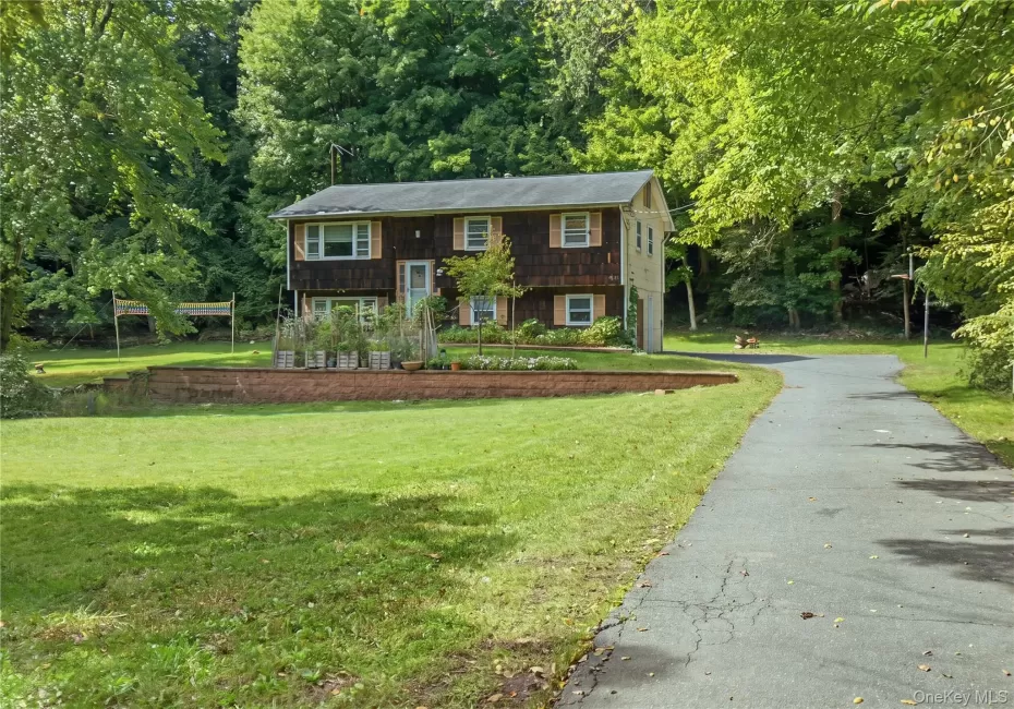 Two-story residence featuring wood-shake siding, shuttered windows, an asphalt driveway, and a tiered brick retaining wall Two-story residence featuring wood-shake siding, shuttered windows, an asphalt driveway, and a tiered brick retaining wall