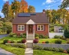 Brick exterior residence featuring solar panels, a gabled roofline, concrete retaining wall, and front entry stairs with a covered portico Brick exterior residence featuring solar panels, a gabled roofline, concrete retaining wall, and front entry stairs with a covered portico