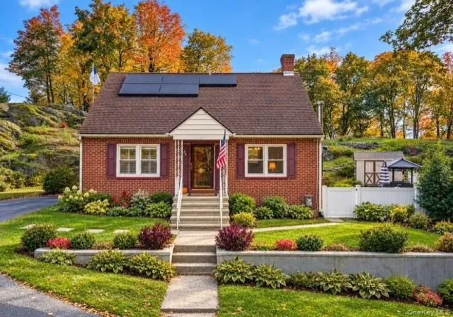 Brick exterior residence featuring solar panels, a gabled roofline, concrete retaining wall, and front entry stairs with a covered portico Brick exterior residence featuring solar panels, a gabled roofline, concrete retaining wall, and front entry stairs with a covered portico