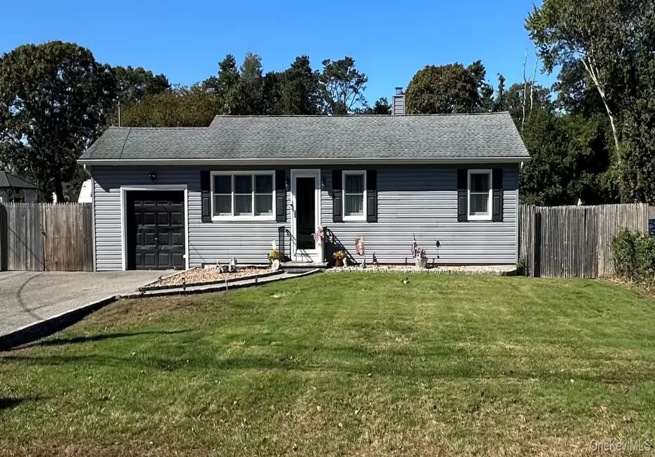 Single-story exterior featuring light-gray horizontal siding, an attached one-car garage, black window shutters, a paved driveway, and perimeter wood fencing Single-story exterior featuring light-gray horizontal siding, an attached one-car garage, black window shutters, a paved driveway, and perimeter wood fencing