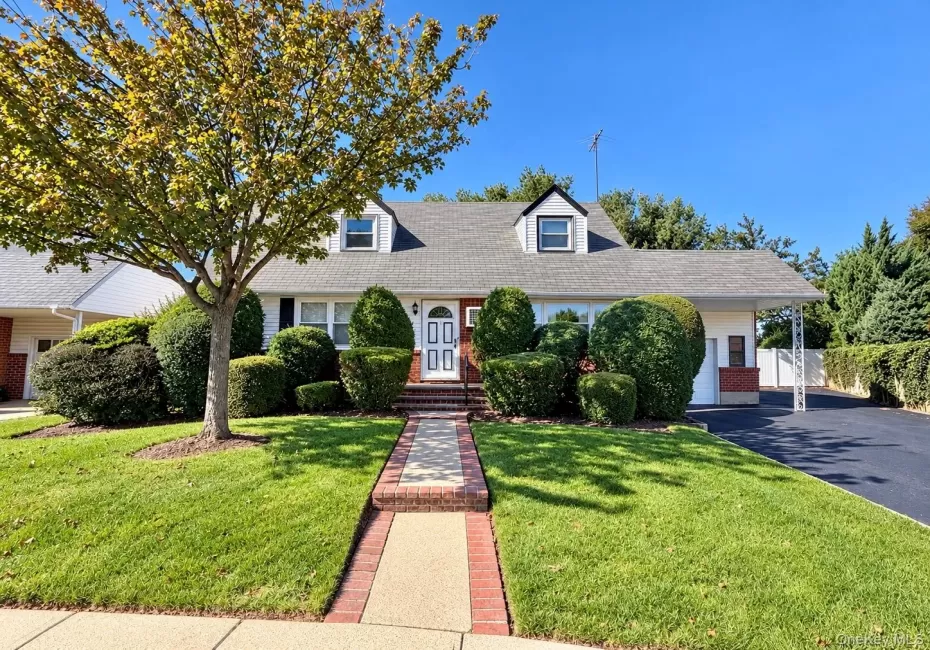 Cape Cod exterior featuring a brick and siding facade, dormer windows, a paved driveway, and an attached carport with decorative iron supports Cape Cod exterior featuring a brick and siding facade, dormer windows, a paved driveway, and an attached carport with decorative iron supports