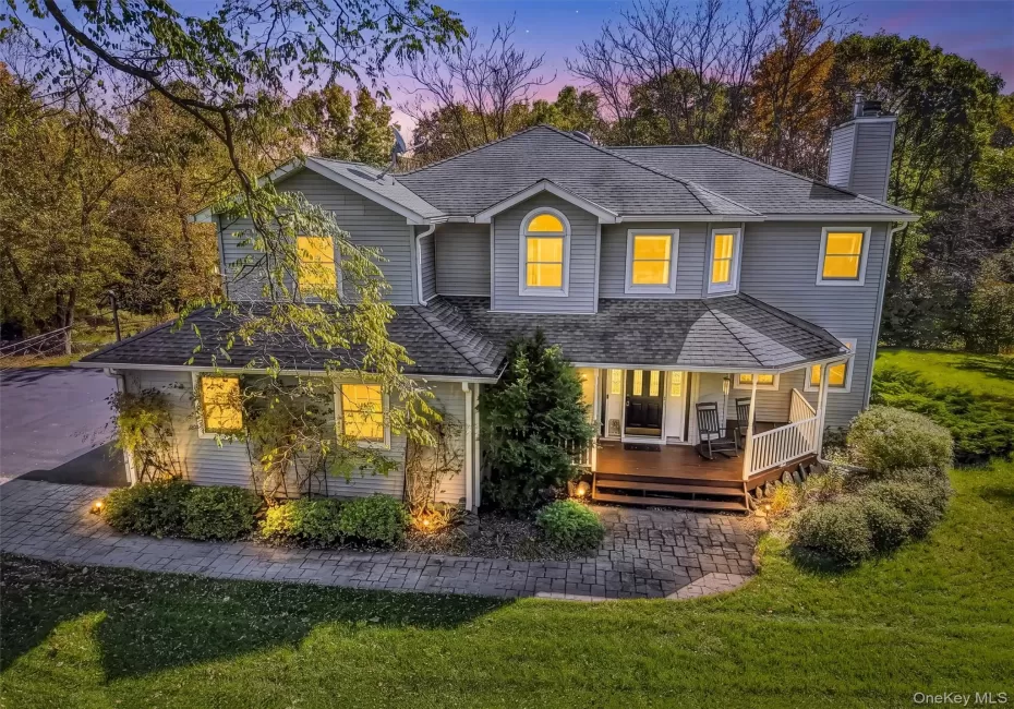 Two-story residence featuring grey horizontal siding, a covered front porch with a white railing, an asphalt shingle roof, a stone-paver walkway. Two-story residence featuring grey horizontal siding, a covered front porch with a white railing, an asphalt shingle roof, a stone-paver walkway.