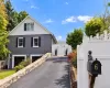 Exterior featuring a two-tone stone and siding facade, an asphalt driveway lined with stone retaining walls, and a white privacy gate Exterior featuring a two-tone stone and siding facade, an asphalt driveway lined with stone retaining walls, and a white privacy gate