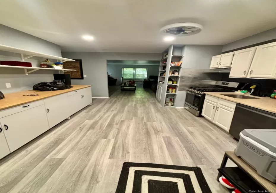 Kitchen featuring light wood-finish flooring, white cabinetry, light countertops, a stainless steel refrigerator, and a dark tile backsplash Kitchen featuring light wood-finish flooring, white cabinetry, light countertops, a stainless steel refrigerator, and a dark tile backsplash