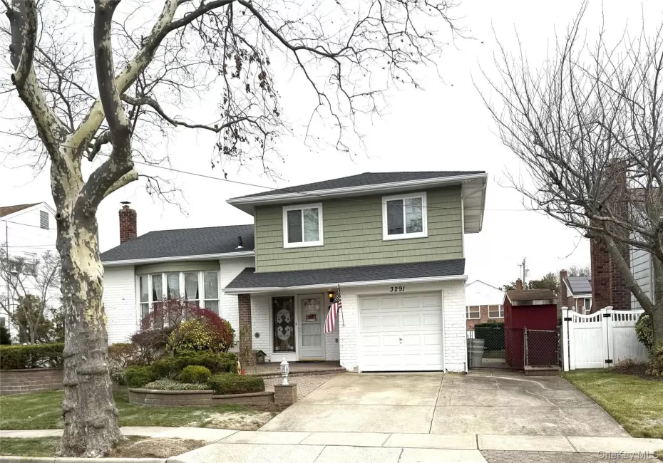 Split level home with a gate, a shingled roof, driveway, brick siding, and a garage Split level home with a gate, a shingled roof, driveway, brick siding, and a garage