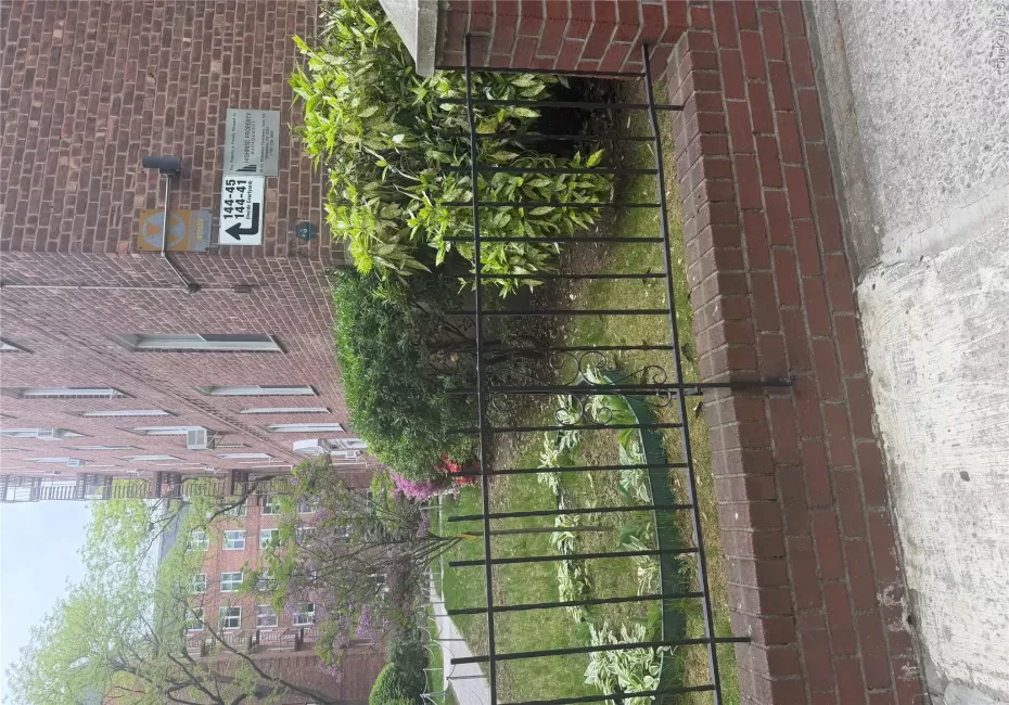 Brick exterior building featuring multiple windows, a black metal fence, mature landscaping, and an adjacent brick building Brick exterior building featuring multiple windows, a black metal fence, mature landscaping, and an adjacent brick building