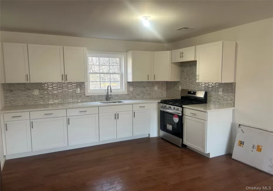 Kitchen#1 with stainless steel gas stove, white cabinetry, dark wood-style flooring, and tasteful backsplash Kitchen#1 with stainless steel gas stove, white cabinetry, dark wood-style flooring, and tasteful backsplash