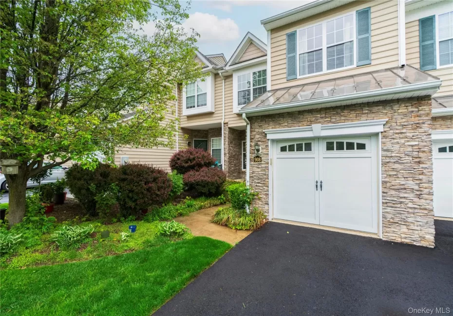 Exterior featuring stacked stone accents, vinyl siding, a two-car garage with paneling and windows, a glass canopy, and established landscaping Exterior featuring stacked stone accents, vinyl siding, a two-car garage with paneling and windows, a glass canopy, and established landscaping