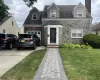 View of front of house featuring a chimney, concrete driveway, a front lawn, roof with shingles, and stone siding View of front of house featuring a chimney, concrete driveway, a front lawn, roof with shingles, and stone siding