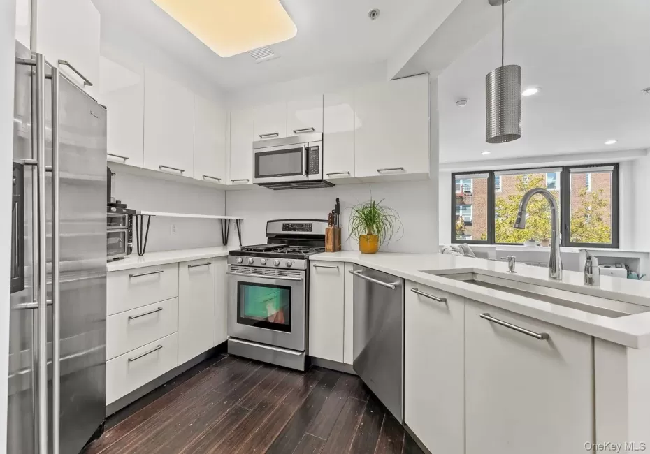 Kitchen featuring white cabinets, appliances with stainless steel finishes, modern cabinets, pendant lighting, and dark wood-style floors Kitchen featuring white cabinets, appliances with stainless steel finishes, modern cabinets, pendant lighting, and dark wood-style floors
