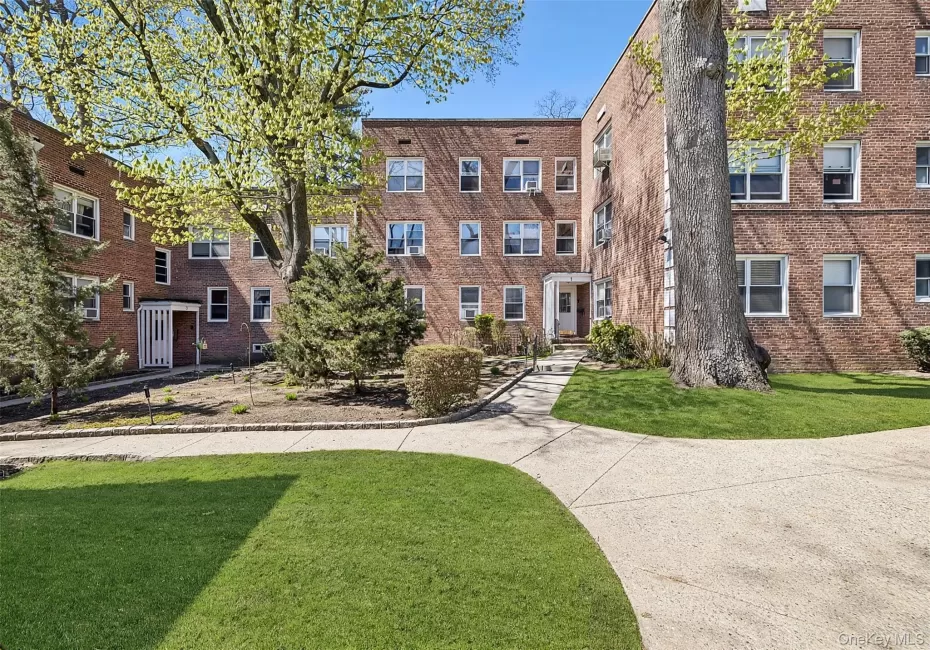 Brick facade residential building with multiple windows, mature trees, manicured lawn, and a concrete pathway leading to the main entrance Brick facade residential building with multiple windows, mature trees, manicured lawn, and a concrete pathway leading to the main entrance