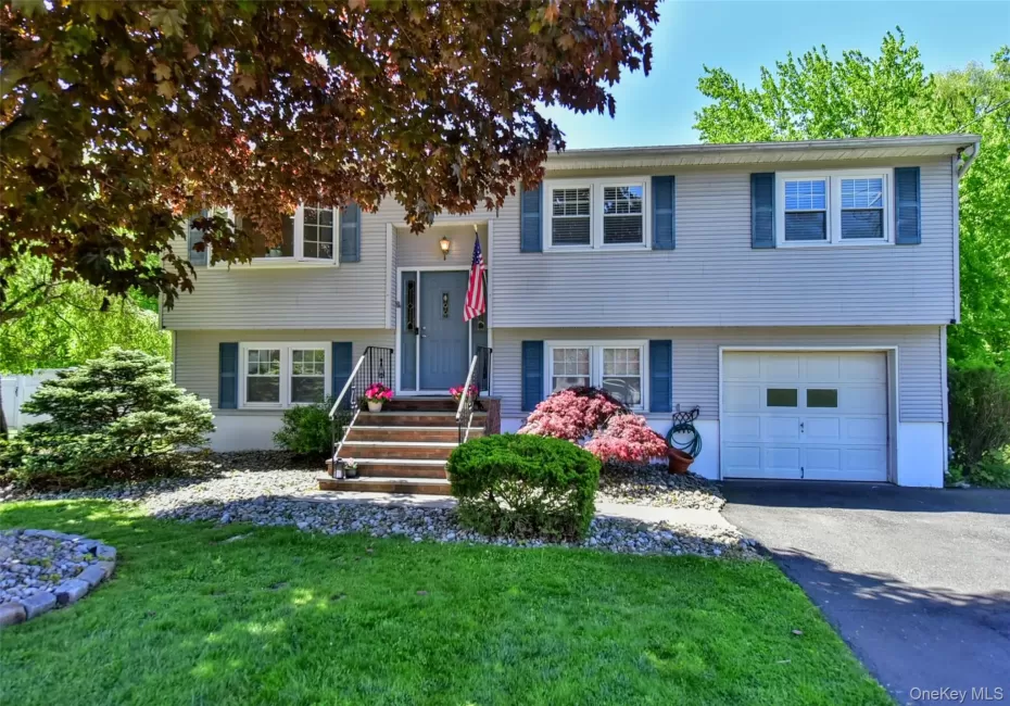 Split-level residence featuring light-colored siding, blue window shutters, metal railings on the front entry, and a one car garage Split-level residence featuring light-colored siding, blue window shutters, metal railings on the front entry, and a one car garage