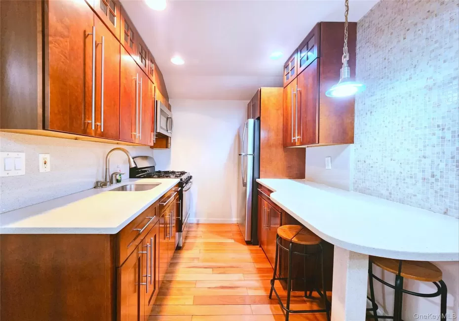 Kitchen featuring brown cabinetry, stainless steel appliances, tasteful backsplash, light wood-type flooring, and a kitchen breakfast bar Kitchen featuring brown cabinetry, stainless steel appliances, tasteful backsplash, light wood-type flooring, and a kitchen breakfast bar