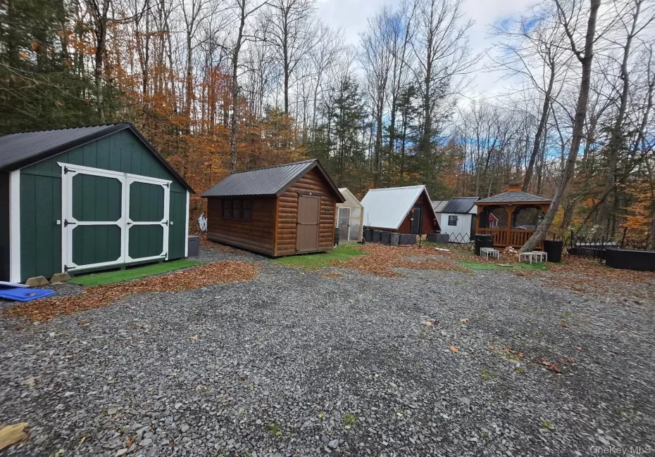 Gravel outdoor area featuring multiple sheds, a small A-frame structure, and a wooden gazebo Gravel outdoor area featuring multiple sheds, a small A-frame structure, and a wooden gazebo
