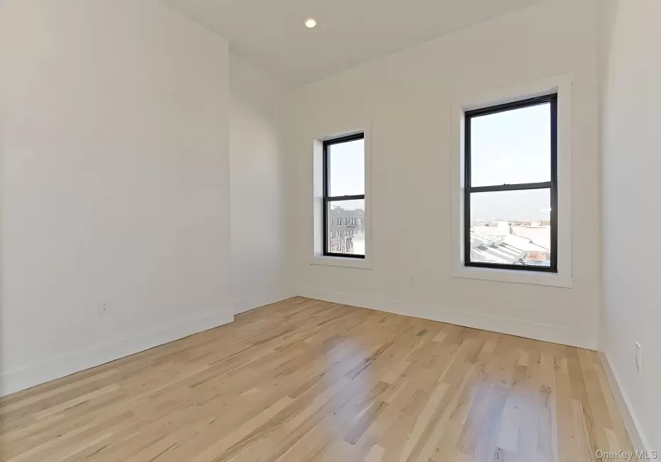 Bright room featuring two large windows with dark frames, light wood-finish flooring, white walls, and recessed lighting Bright room featuring two large windows with dark frames, light wood-finish flooring, white walls, and recessed lighting