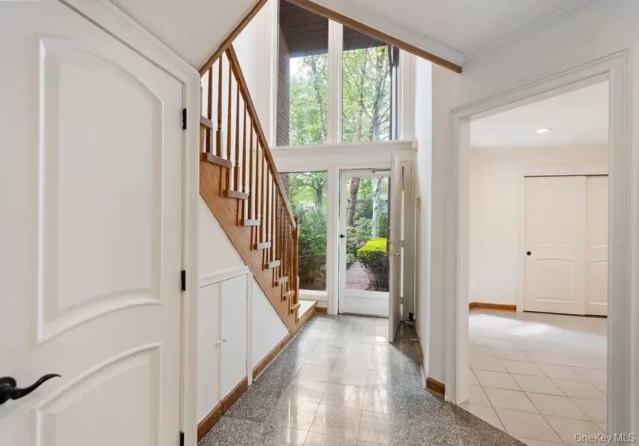 Foyer featuring a grand staircase with wood treads and railings, expansive floor-to-ceiling windows, and a tiled floor Foyer featuring a grand staircase with wood treads and railings, expansive floor-to-ceiling windows, and a tiled floor