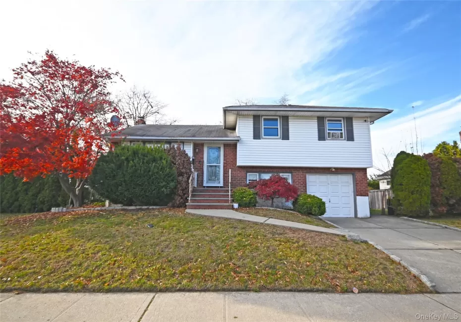 Tri-level home featuring brick siding, concrete driveway, a front lawn, a garage, and a chimney Tri-level home featuring brick siding, concrete driveway, a front lawn, a garage, and a chimney