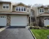 Exterior view of the property showcasing tan siding, stone accents, and a paved driveway leading to a two-car garage Exterior view of the property showcasing tan siding, stone accents, and a paved driveway leading to a two-car garage