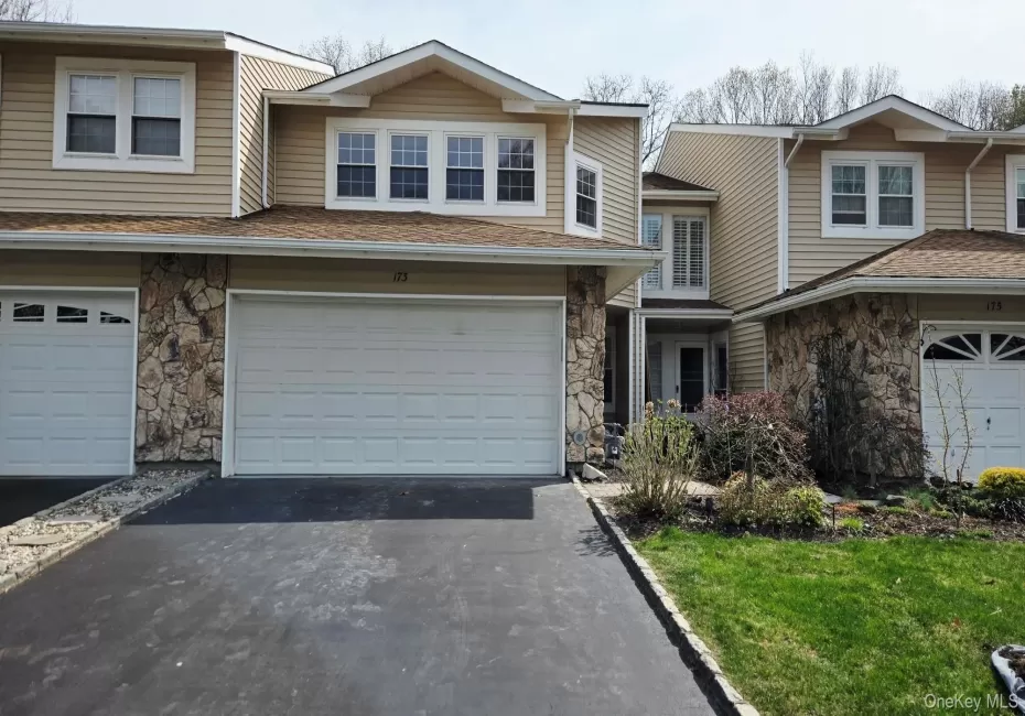 Exterior view of the property showcasing tan siding, stone accents, and a paved driveway leading to a two-car garage Exterior view of the property showcasing tan siding, stone accents, and a paved driveway leading to a two-car garage
