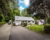 View of front of property featuring asphalt driveway, a front yard, a shingled roof, and view of wooded area View of front of property featuring asphalt driveway, a front yard, a shingled roof, and view of wooded area