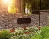 Stone entrance wall with a dark metal plaque, featuring manicured flower beds and established greenery Stone entrance wall with a dark metal plaque, featuring manicured flower beds and established greenery