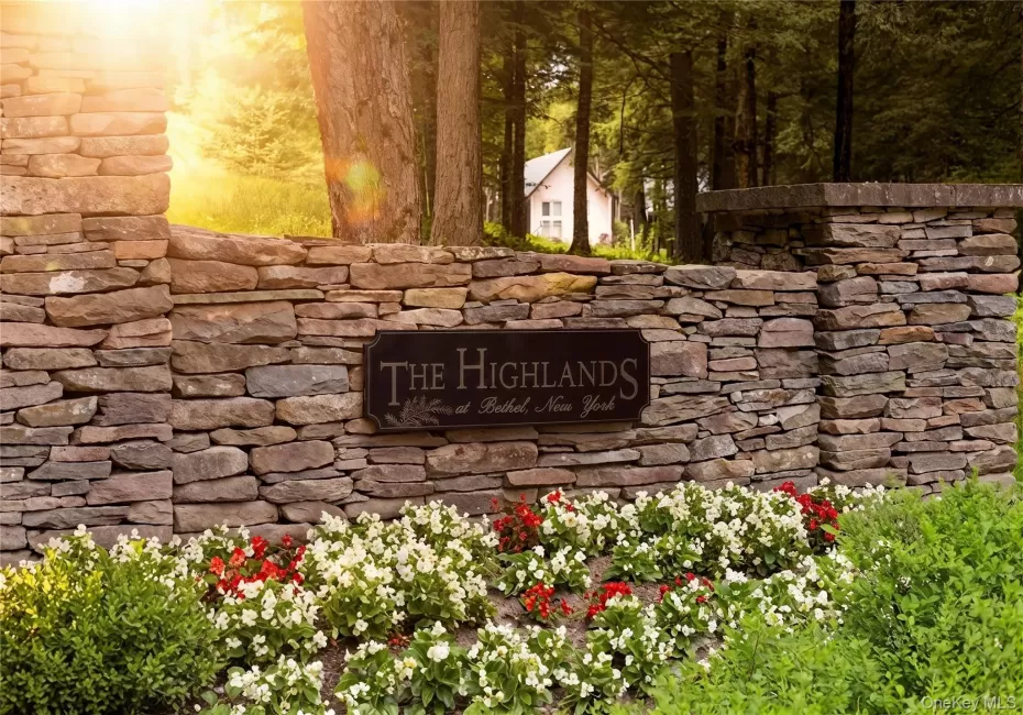 Stone entrance wall with a dark metal plaque, featuring manicured flower beds and established greenery Stone entrance wall with a dark metal plaque, featuring manicured flower beds and established greenery