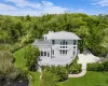 Contemporary residence with a multi-level exterior, featuring multiple balconies, a gravel driveway, mature perimeter landscaping, and a manicured lawn Contemporary residence with a multi-level exterior, featuring multiple balconies, a gravel driveway, mature perimeter landscaping, and a manicured lawn