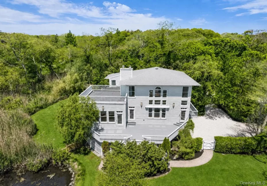 Contemporary residence with a multi-level exterior, featuring multiple balconies, a gravel driveway, mature perimeter landscaping, and a manicured lawn Contemporary residence with a multi-level exterior, featuring multiple balconies, a gravel driveway, mature perimeter landscaping, and a manicured lawn
