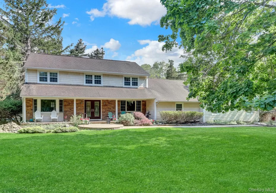 Expansive green lawn fronts a two-story residence featuring light-colored siding and a covered front porch with stone facade accents Expansive green lawn fronts a two-story residence featuring light-colored siding and a covered front porch with stone facade accents