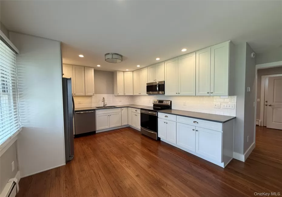 Kitchen with dark wood-style flooring, stainless steel appliances, a baseboard heating unit, and a sink Kitchen with dark wood-style flooring, stainless steel appliances, a baseboard heating unit, and a sink