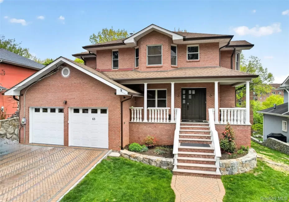 Brick exterior residence featuring a two-car garage, paved driveway, and covered front porch with white balustrades Brick exterior residence featuring a two-car garage, paved driveway, and covered front porch with white balustrades