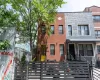 Brick facade townhome featuring a vibrant yellow entry door, black security bars on windows, and a multi-level black fence Brick facade townhome featuring a vibrant yellow entry door, black security bars on windows, and a multi-level black fence