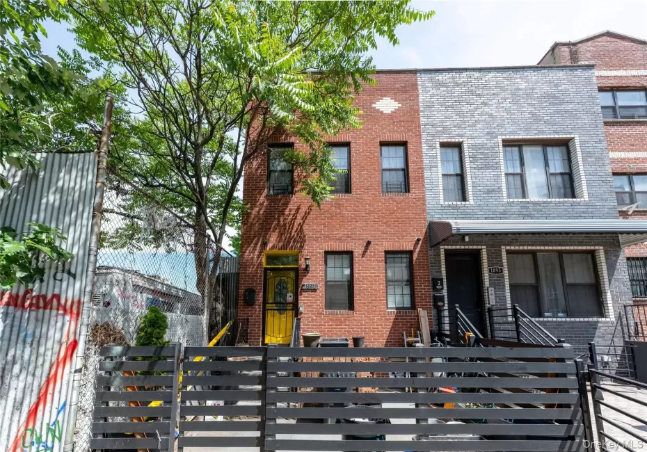 Brick facade townhome featuring a vibrant yellow entry door, black security bars on windows, and a multi-level black fence Brick facade townhome featuring a vibrant yellow entry door, black security bars on windows, and a multi-level black fence