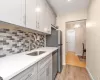 Kitchen featuring light gray cabinetry with brushed nickel pulls, a stainless steel sink with a gooseneck faucet, white solid surface countertops, and a mosaic tile backsplash Kitchen featuring light gray cabinetry with brushed nickel pulls, a stainless steel sink with a gooseneck faucet, white solid surface countertops, and a mosaic tile backsplash