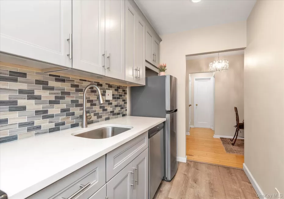 Kitchen featuring light gray cabinetry with brushed nickel pulls, a stainless steel sink with a gooseneck faucet, white solid surface countertops, and a mosaic tile backsplash Kitchen featuring light gray cabinetry with brushed nickel pulls, a stainless steel sink with a gooseneck faucet, white solid surface countertops, and a mosaic tile backsplash