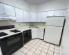 Kitchen with black appliances, light countertops, white cabinets, under cabinet range hood, and light tile patterned flooring Kitchen with black appliances, light countertops, white cabinets, under cabinet range hood, and light tile patterned flooring