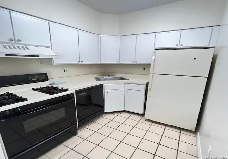 Kitchen with black appliances, light countertops, white cabinets, under cabinet range hood, and light tile patterned flooring Kitchen with black appliances, light countertops, white cabinets, under cabinet range hood, and light tile patterned flooring