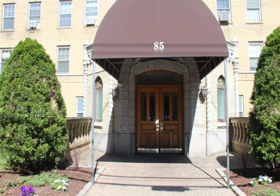 Building entrance featuring a prominent arched doorway, double wooden entry doors, and a brown canvas awning Building entrance featuring a prominent arched doorway, double wooden entry doors, and a brown canvas awning