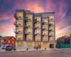 Modern multi-story building featuring a brick and panel facade, individual balconies with glass railings, large windows, an integrated ground-floor entrance, and a covered parking area Modern multi-story building featuring a brick and panel facade, individual balconies with glass railings, large windows, an integrated ground-floor entrance, and a covered parking area